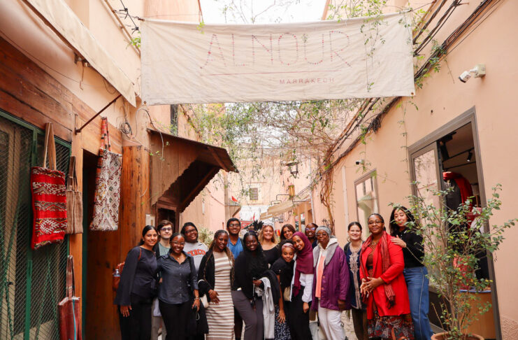 A group of people pose together in an outdoor hallway beneath a large banner reading Alnour Marrakech.