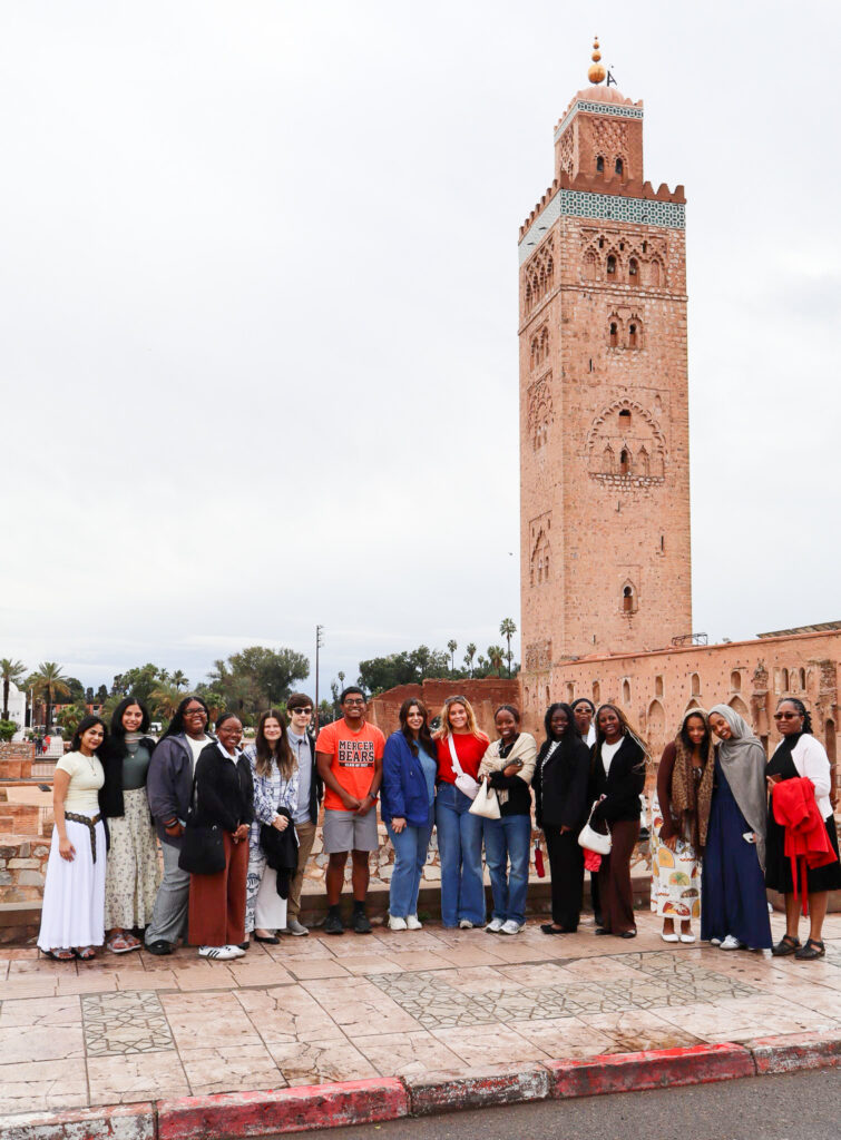 A group of people poses in front of the Koutoubia Mosque in Marrakesh, Morocco, on a cloudy day.