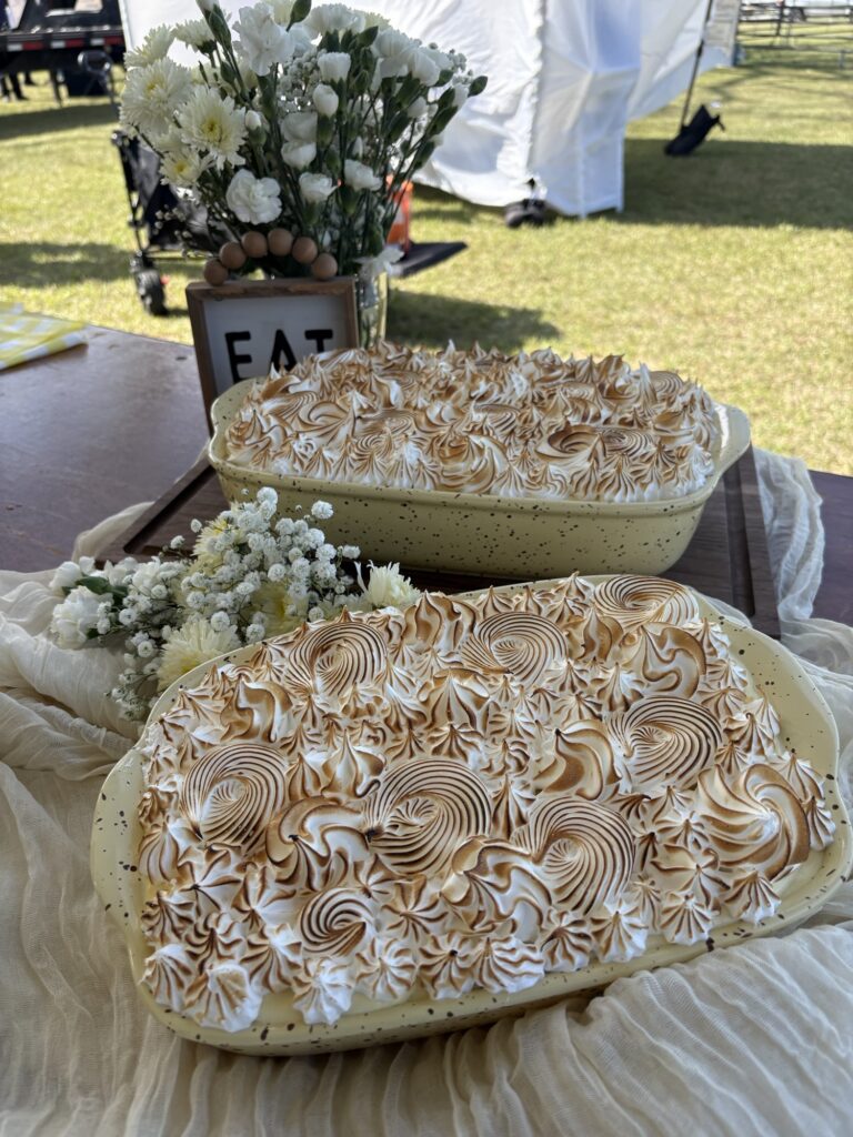 Two rectangular pies with browned meringue topping on a table, with flowers and a small “EAT” sign in the background.