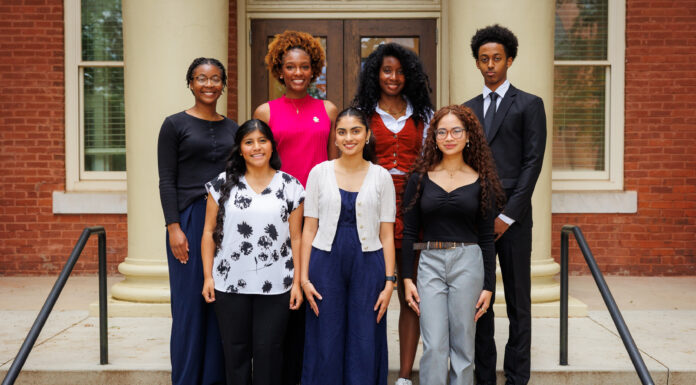 Twelve students selected to study abroad as Gilman Scholars Seven people stand in two rows on steps outside a brick building with columns, facing the camera and smiling.