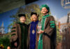 Outstanding School of Medicine graduates and faculty honored during 2026 commencement Three people in academic regalia pose on stage at a graduation ceremony; one holds a glass award and smiles.