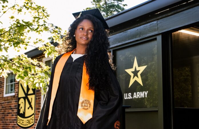 Beyoncé Francis in a graduation gown and cap stands in front of a U.S. Army sign.