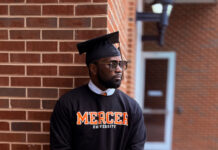 Graduate Spotlight: Deon Brown A man in a graduation cap and Mercer University sweatshirt leans against a brick wall outdoors.