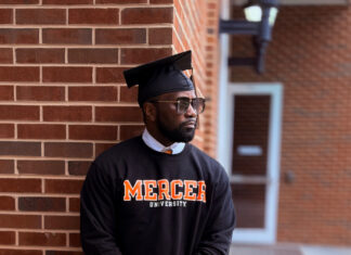 Graduate Spotlight: Deon Brown A man in a graduation cap and Mercer University sweatshirt leans against a brick wall outdoors.