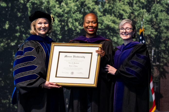 Three women in academic regalia hold a framed Mercer University diploma at a graduation ceremony.