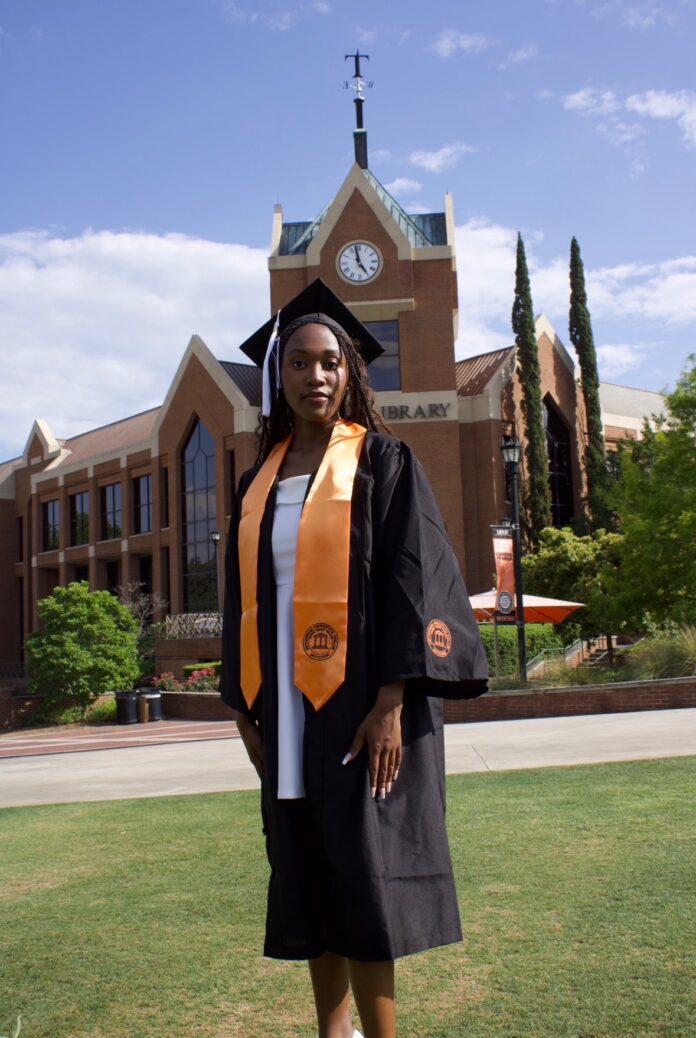 Olivia Harris in cap and gown stands on grass in front of Tarver Library.