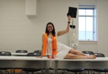 Graduate Spotlight: Virginia Fox A woman in graduation attire poses on a table, holding a cap, with a skeleton model in the background.