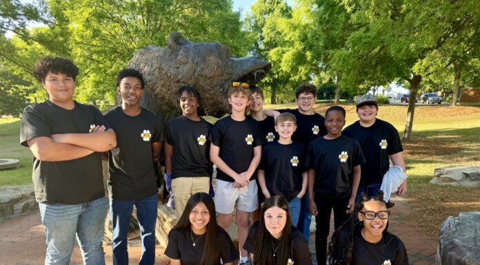 Education alumna brings middle schoolers to Mercer campus for robotics contest A group of students in matching black shirts poses in front of a bear statue outdoors on a sunny day.