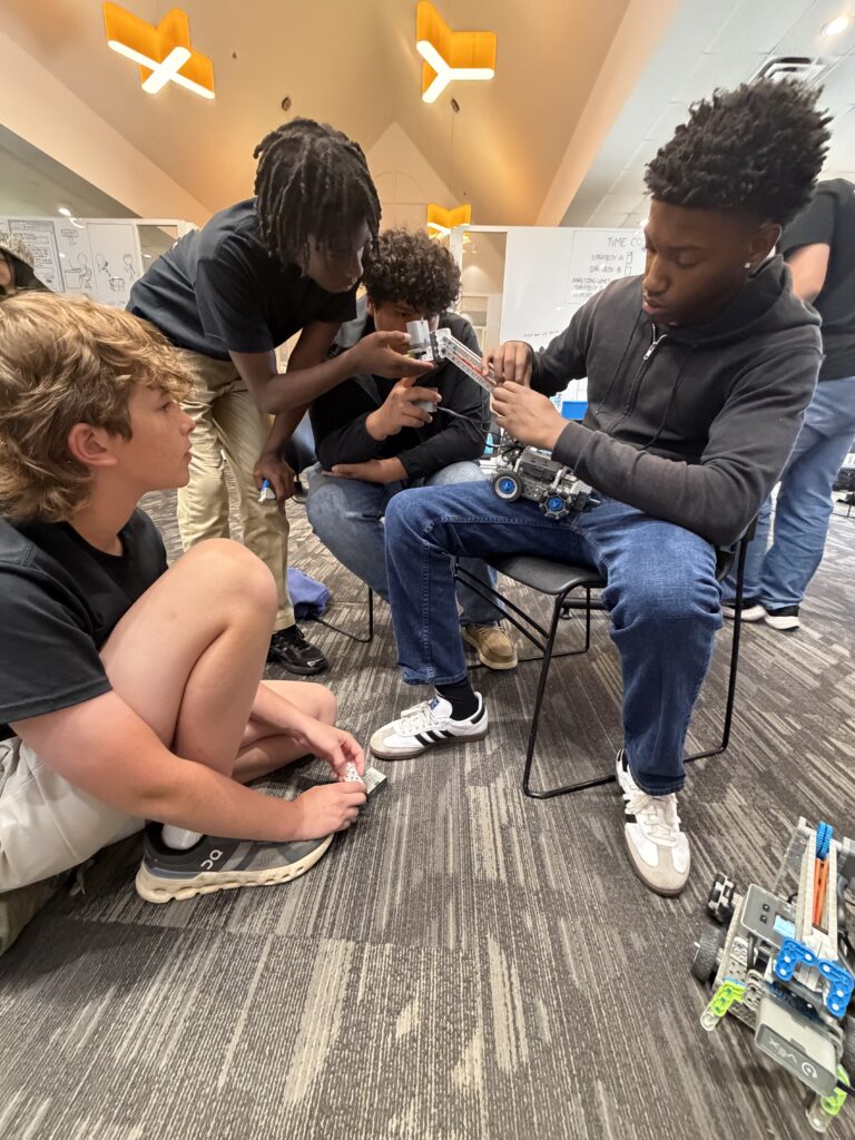 Four teenagers work together on assembling a robotics project in a classroom setting.