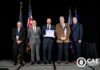 Mercer formally receives NSA Center of Academic Excellence designation Five men in suits stand on stage with flags, one holding a certificate; CAE in Cybersecurity Community logo is visible.