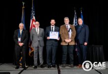 Mercer formally receives NSA Center of Academic Excellence designation Five men in suits stand on stage with flags, one holding a certificate; CAE in Cybersecurity Community logo is visible.