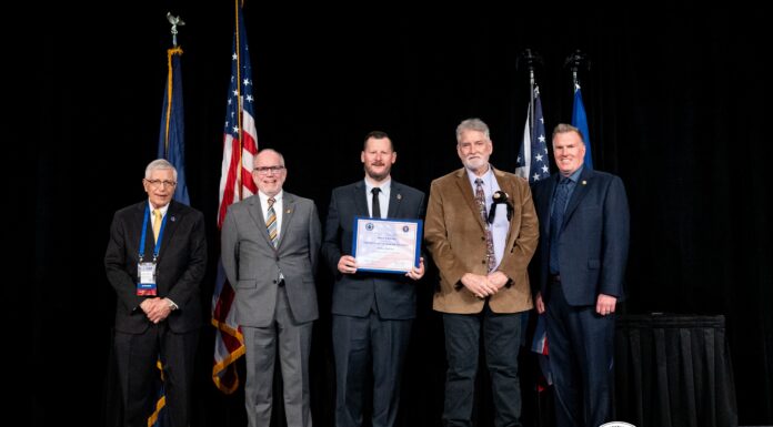 Mercer formally receives NSA Center of Academic Excellence designation Five men in suits stand on stage with flags, one holding a certificate; CAE in Cybersecurity Community logo is visible.