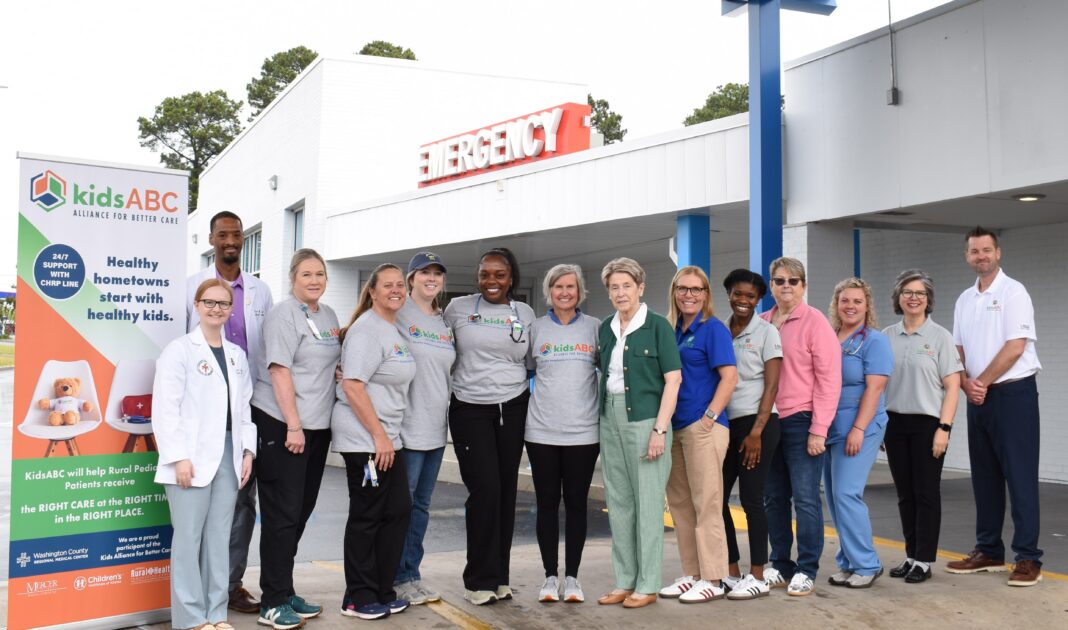 A group of people stands in front of an emergency entrance, posing for a photo next to a kidsABC sign.