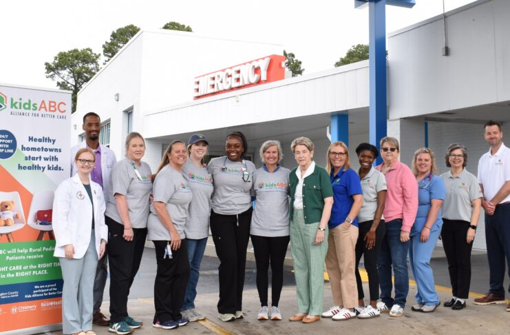 A group of people stands in front of an emergency entrance, posing for a photo next to a kidsABC sign.