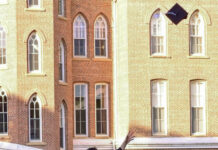 Graduate Spotlight: Andrew Halliburton Graduate in cap and gown throws graduation cap into the air in front of a brick academic building.