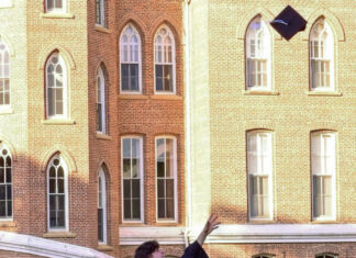 Graduate Spotlight: Andrew Halliburton Graduate in cap and gown throws graduation cap into the air in front of a brick academic building.