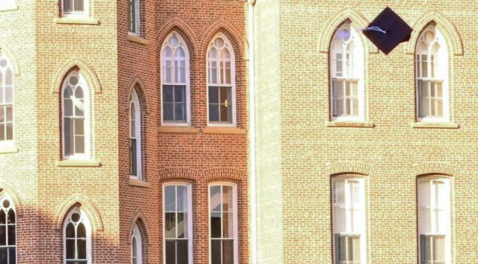 Graduate Spotlight: Andrew Halliburton Graduate in cap and gown throws graduation cap into the air in front of a brick academic building.