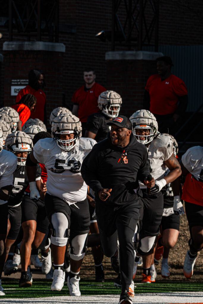 Joel Taylor leads Mercer football players as they run together on a field during practice.