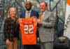 New head coach readies Mercer football for historic run President Dr. Penny L. Elkins, Joel Taylor and Jim Cole pose indoors as Joel Taylor holds a Mercer University football jersey labeled Taylor 22.