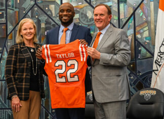 New head coach readies Mercer football for historic run President Dr. Penny L. Elkins, Joel Taylor and Jim Cole pose indoors as Joel Taylor holds a Mercer University football jersey labeled Taylor 22.