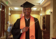 Graduate Spotlight: Michael Bloom A graduate in cap and gown with an orange stole holds a conductors baton, standing indoors and smiling at the camera.
