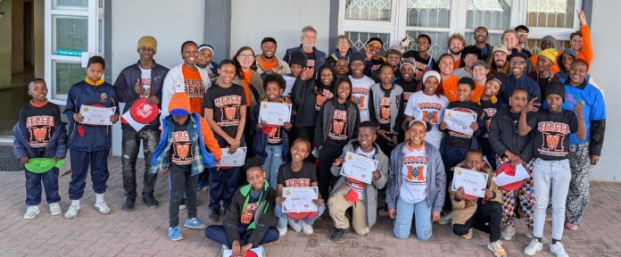 Bob Allen with MOM group A large group of children and adults pose together outside a building, holding certificates and wearing matching shirts.