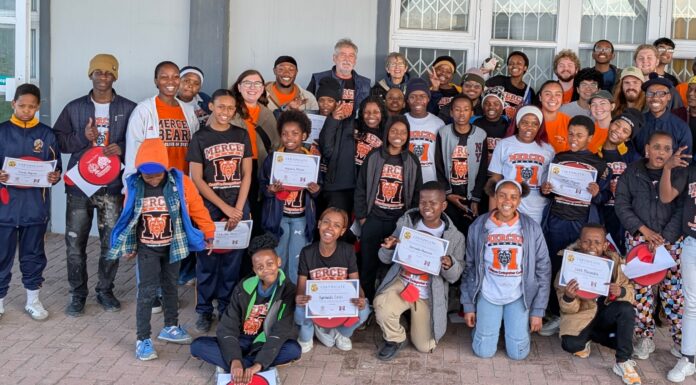 Professor earns EXPy Award for computer science initiatives at home and abroad A large group of children and adults pose together outside a building, holding certificates and wearing matching shirts.