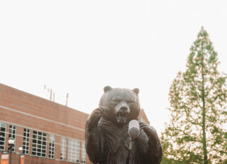 Graduate Spotlight: Pariss Nicholson Pariss Nicholson in cap and gown poses playfully with a microphone in front of the bear statue at Mercer.