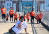 Graduate Spotlight: Pauline Wilder A group of children and one adult pose on a bridge, all wearing orange T-shirts except the seated woman in white.