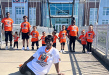 Graduate Spotlight: Pauline Wilder A group of children and one adult pose on a bridge, all wearing orange T-shirts except the seated woman in white.