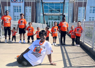 Graduate Spotlight: Pauline Wilder A group of children and one adult pose on a bridge, all wearing orange T-shirts except the seated woman in white.