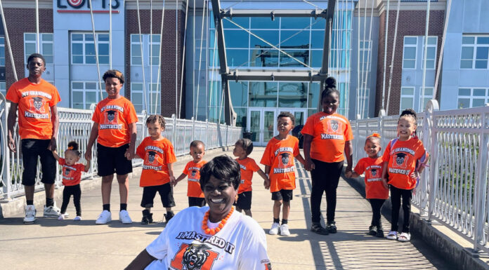 Graduate Spotlight: Pauline Wilder A group of children and one adult pose on a bridge, all wearing orange T-shirts except the seated woman in white.