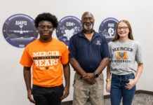 Engineering alumnus helps keep Air Force aircraft flying Three people stand indoors in front of wall signs, two wearing Mercer University shirts and one in a navy polo.