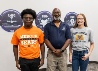 Engineering alumnus helps keep Air Force aircraft flying Three people stand indoors in front of wall signs, two wearing Mercer University shirts and one in a navy polo.