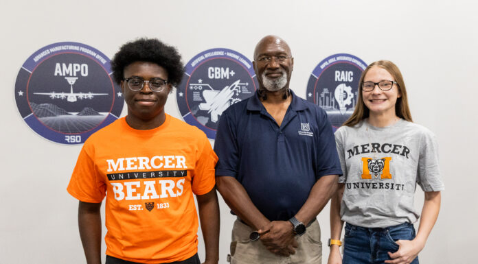 Engineering alumnus helps keep Air Force aircraft flying Three people stand indoors in front of wall signs, two wearing Mercer University shirts and one in a navy polo.