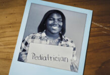 From fifth grade dream to future rural pediatrician Caitlyn holding a sign that says Pediatrician in a black and white photo on a wooden surface.
