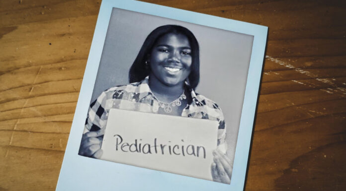 From fifth grade dream to future rural pediatrician Caitlyn holding a sign that says Pediatrician in a black and white photo on a wooden surface.