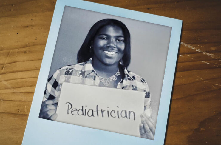 Caitlyn holding a sign that says Pediatrician in a black and white photo on a wooden surface.