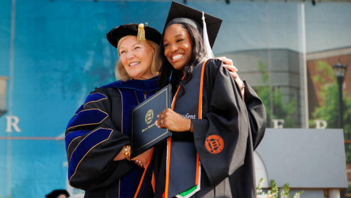 Charity Obazughanmwen and Dr Elkins A graduate and faculty member in academic regalia smile and pose together at a graduation ceremony.