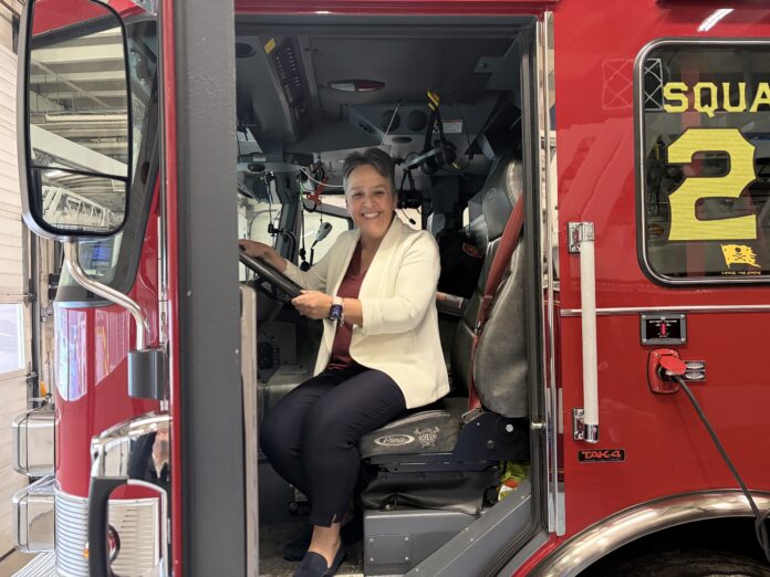 Katie Davis sits in the driver’s seat of a red fire truck inside a fire station.