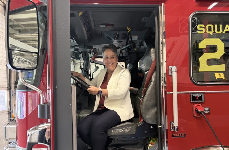 Katie Davis sits in the driver’s seat of a red fire truck inside a fire station.