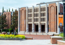 Mercer team develops innovative tools for analyzing climate data Brick building with three entrances, decorative façade, and flowerbeds in front; orange banner on the right.