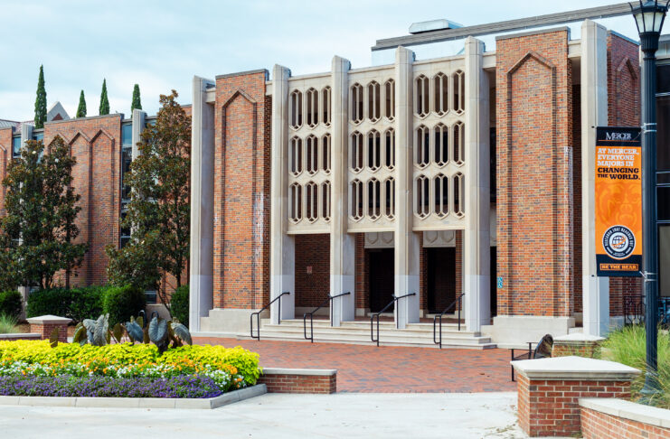 Brick building with three entrances, decorative façade, and flowerbeds in front; orange banner on the right.