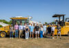 Students see engineering in practice at medical school construction site A group of people standing outdoors in front of large construction vehicles under a clear blue sky.