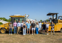 Students see engineering in practice at medical school construction site A group of people standing outdoors in front of large construction vehicles under a clear blue sky.