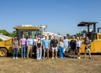 Students see engineering in practice at medical school construction site A group of people standing outdoors in front of large construction vehicles under a clear blue sky.