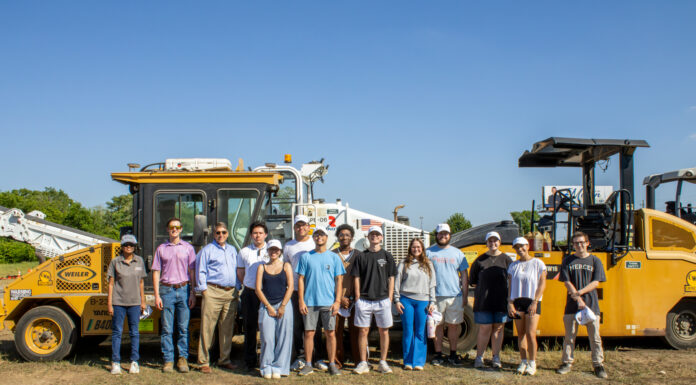 Students see engineering in practice at medical school construction site A group of people standing outdoors in front of large construction vehicles under a clear blue sky.