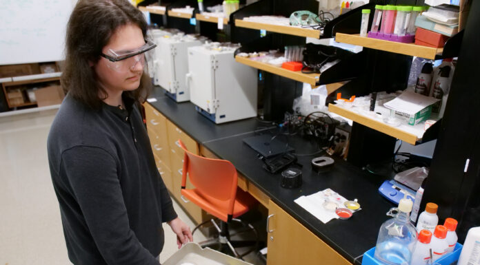 Mercer professors develop international standard for detecting lead in new paint Person in safety glasses uses a handheld device to scan paint samples on a cart in a laboratory setting.