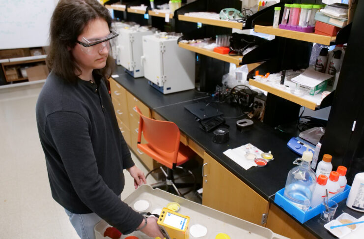 Person in safety glasses uses a handheld device to scan paint samples on a cart in a laboratory setting.