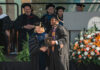 Mercer scholar-athlete Bears post record year in the classroom Graduate in cap and gown shakes hands with faculty member on stage at a commencement ceremony with flowers nearby.